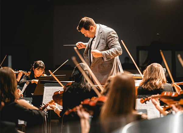 Person conducting in front of full orchestra with Manahsset stands